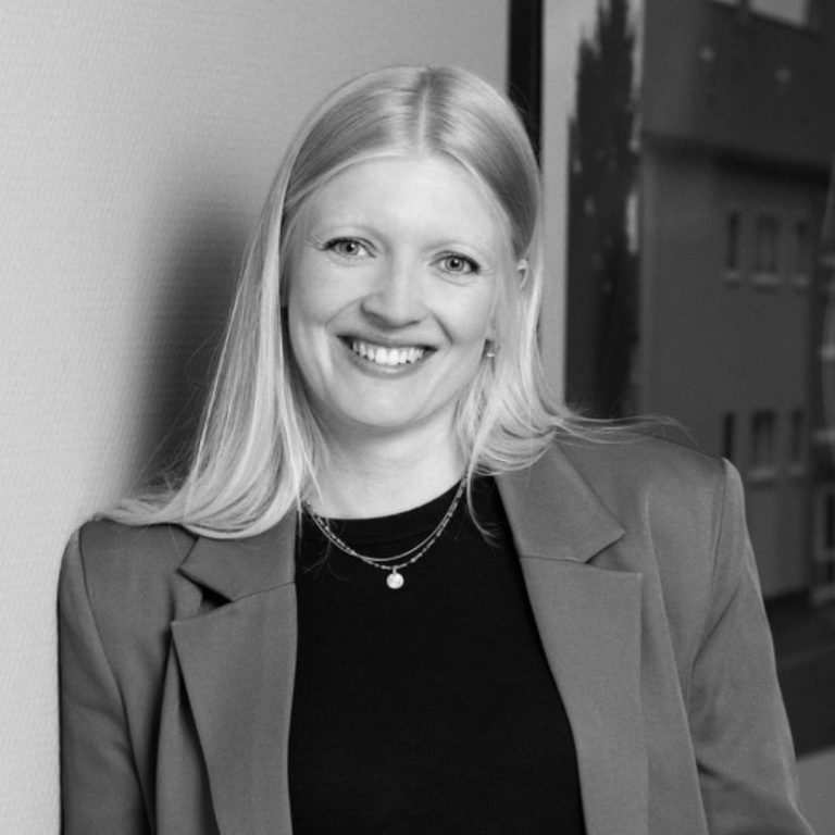 Lisa Potthoff Lächelnde Frau mit blonden Haaren, in einem Blazer, vor einem grauen Hintergrund.