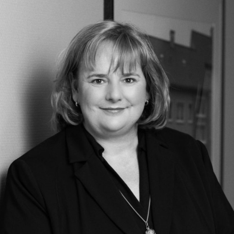 Antje Grundmann Porträt einer Frau mit schulterlangen, lockigen Haaren, in schwarzer Blazerjacke.
