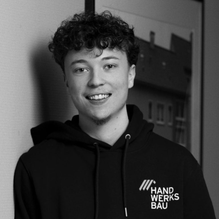 Lächelnder Jugendlicher mit lockigem Haar in einem schwarzen Hoodie vor einem Hintergrund.