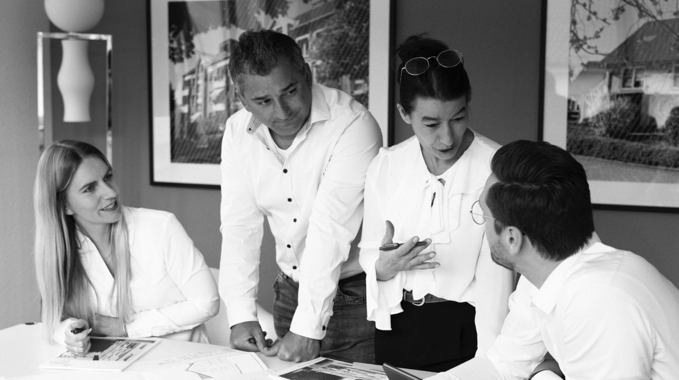 Vier Personen stehen um einen Computerbildschirm und lächeln.